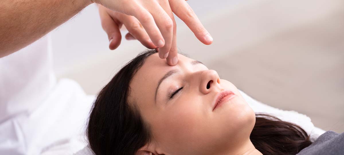 Person laying down with eyes closed therapists fingertip on forehead