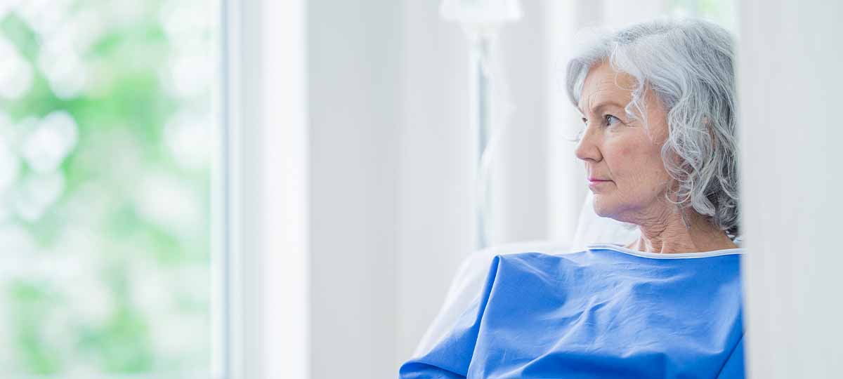 Older person in hospital gown looking out window