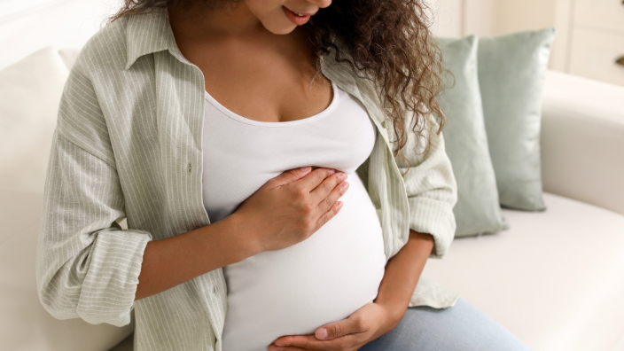an image of a pregnant woman looking at her stomach and smiling.