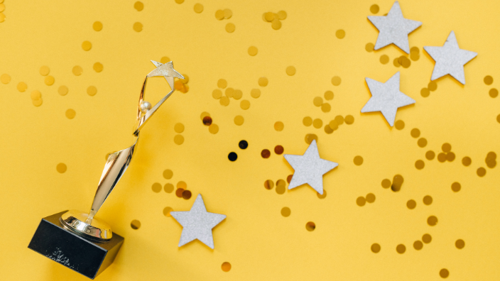 an image of a trophy on a tellowbackground with gold stars around it.