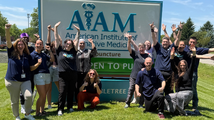 an image of massage school students posing in front of the school sign.