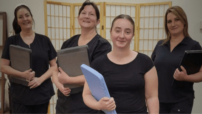 Students all in black, holding clipboards, posing for camera