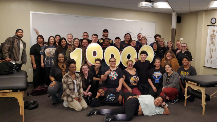 an image of a group of people smiling in a classroom, they hold a sign that saying $10,000 on it.