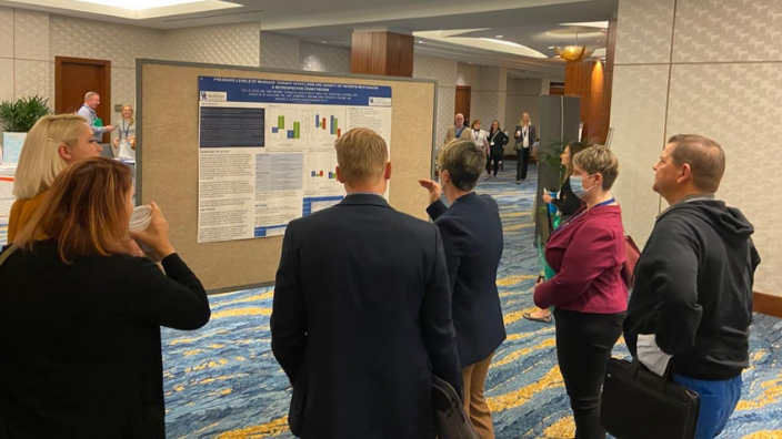 an image of a group of people listening to a woman explain her research poster.