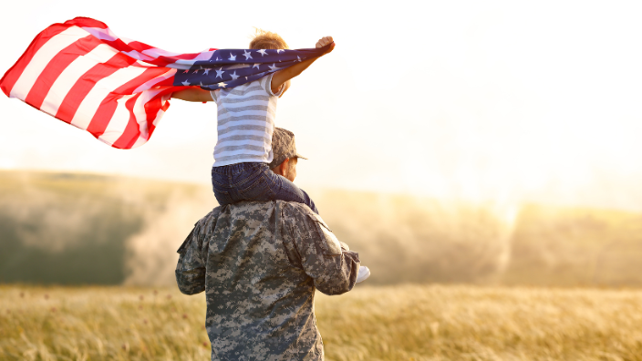 an image of a veteran holding a child on their shoulders, as they wave the American flag.