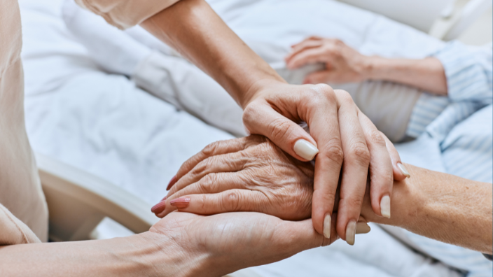 an image of two hands holding the hand on someone in a hospital bed.
