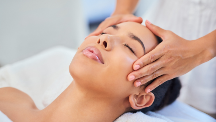 A close up image of a woman's serene face as she relieves a scalp massage by a massage therapist.