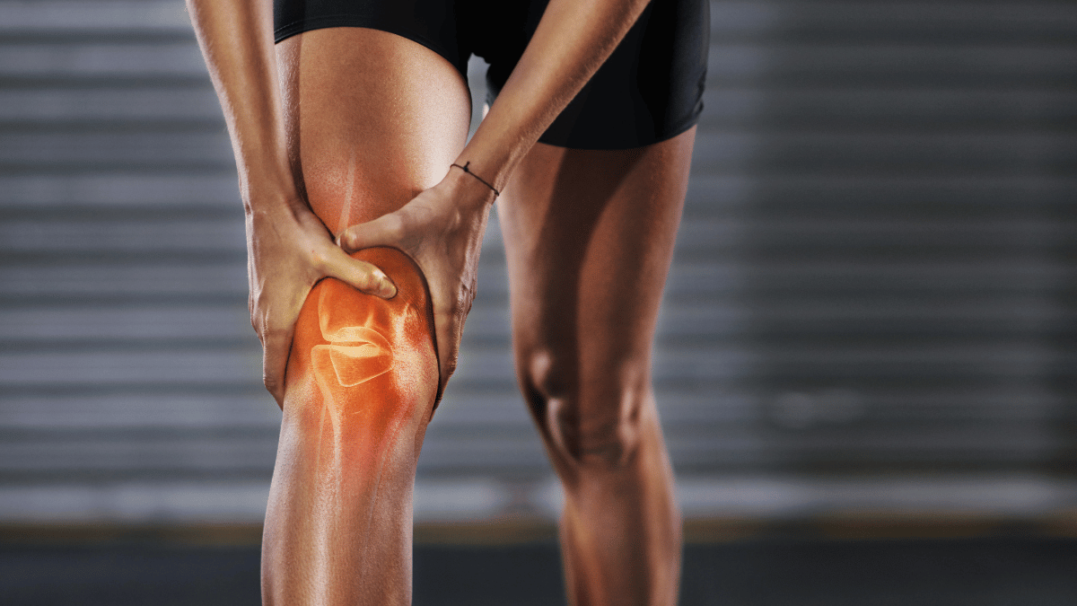 An image of someone grabbing their knee in pain, the image shows an x-ray of the bones in the knee.
