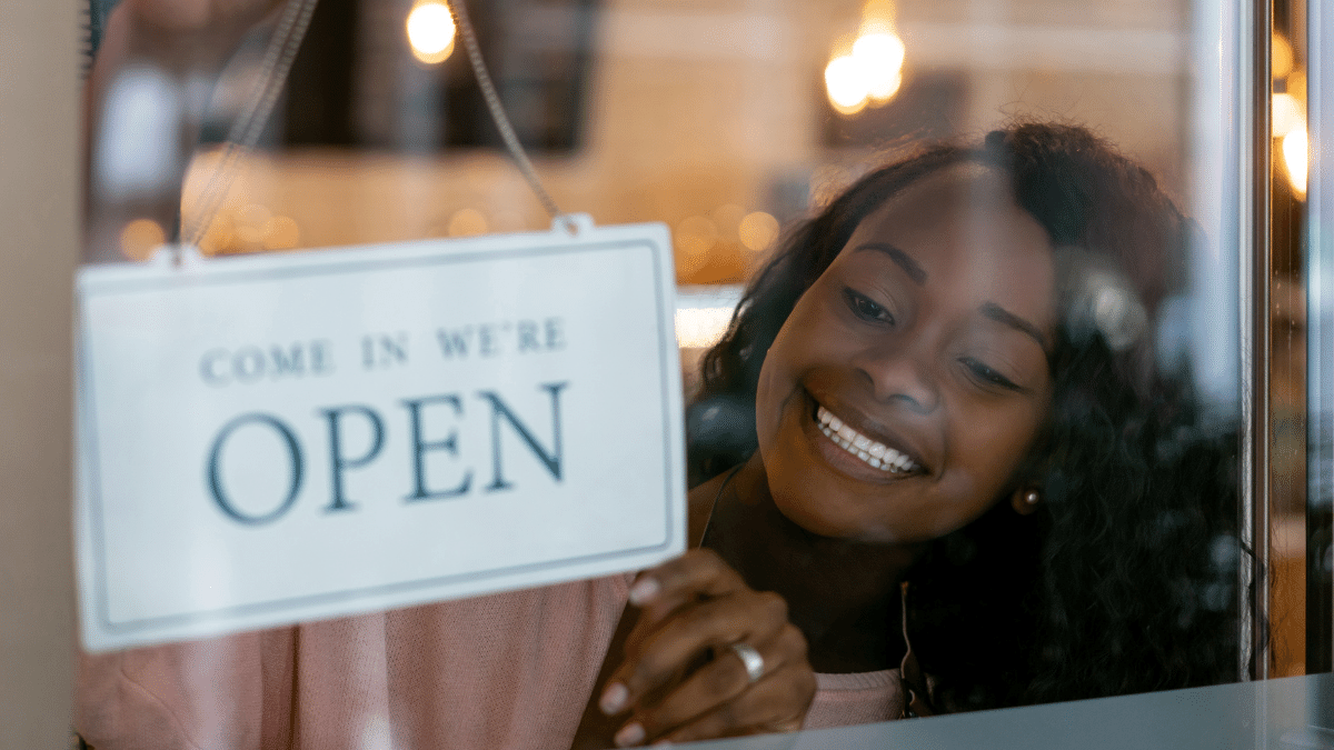 an image of a woman putting up an "open" sign for her business.