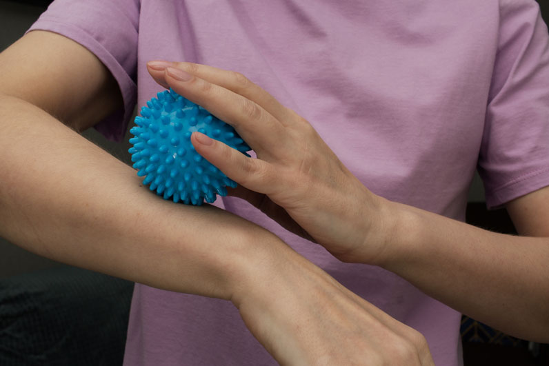 woman rolling massage ball on forearm