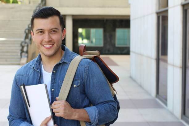 male student smiling with notebook in arms